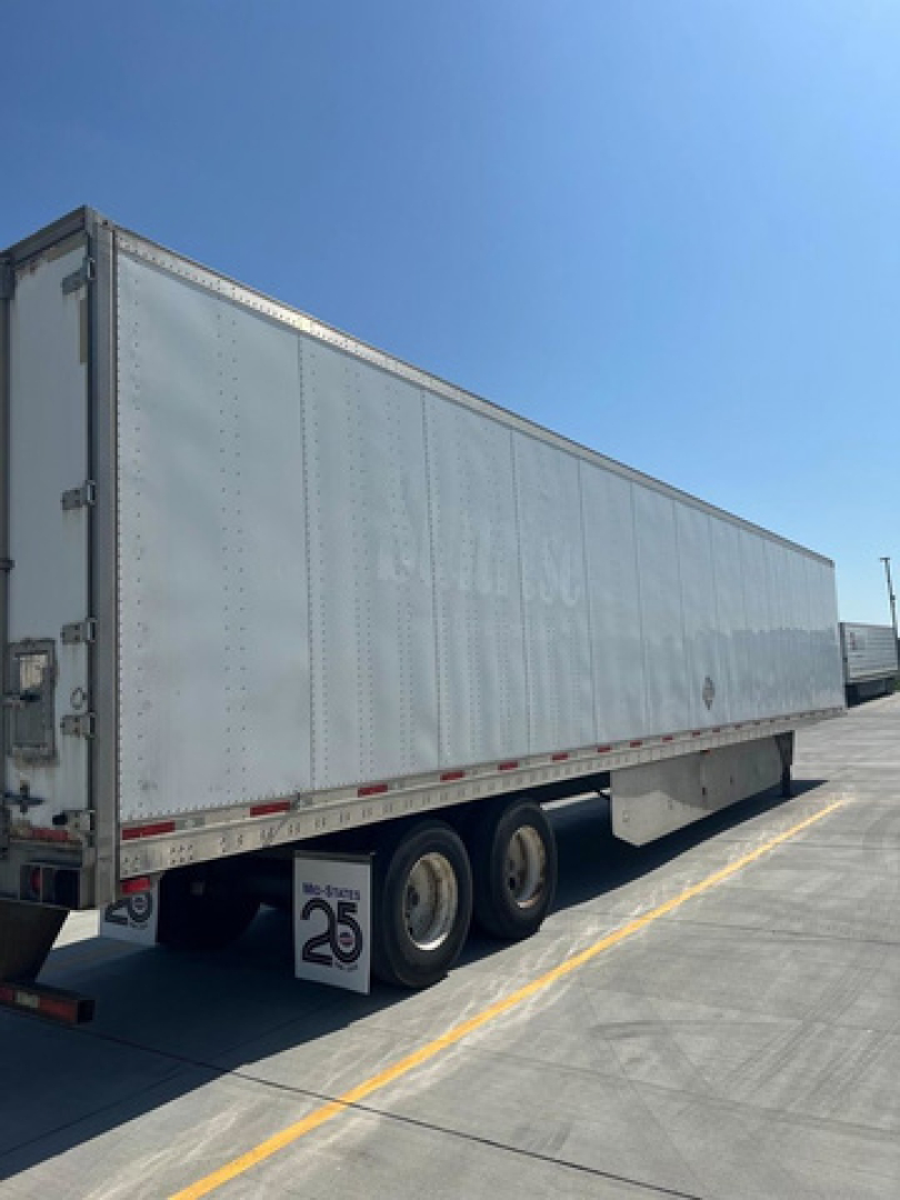 Trailer side view showing a long silver utility van/trailer with dual rear tires and a ribbed aluminum exterior. No visible text legible on the side.