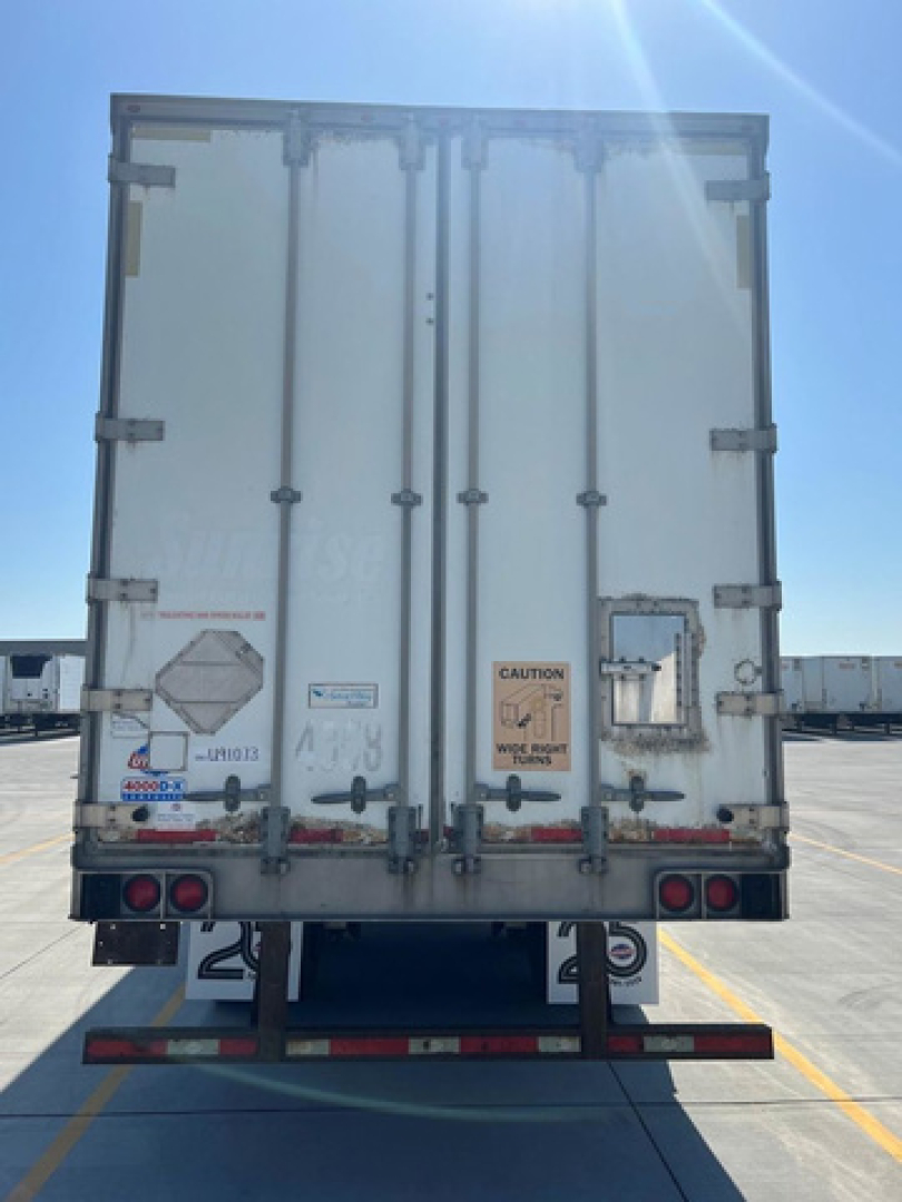 Rear view of a white cargo trailer with double doors, warning stickers, and taillights in a parking lot.