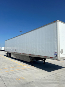 Trailered utility van trailer with plain aluminum side, undercarriage shows two axles and support legs; no visible text on side apart from small reflective diamonds and numbers near rear.
