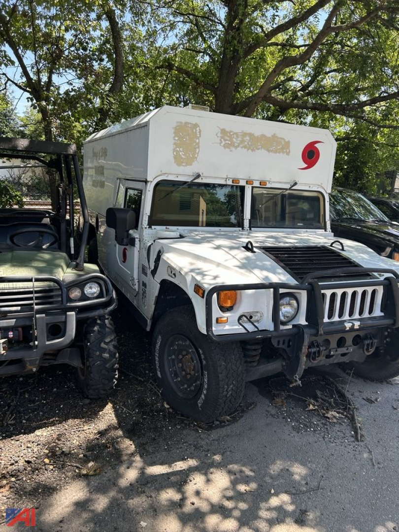 Hummer H1 utility truck in a parking lot showing front cab and raised camper bed with stickers and wheel arches.
