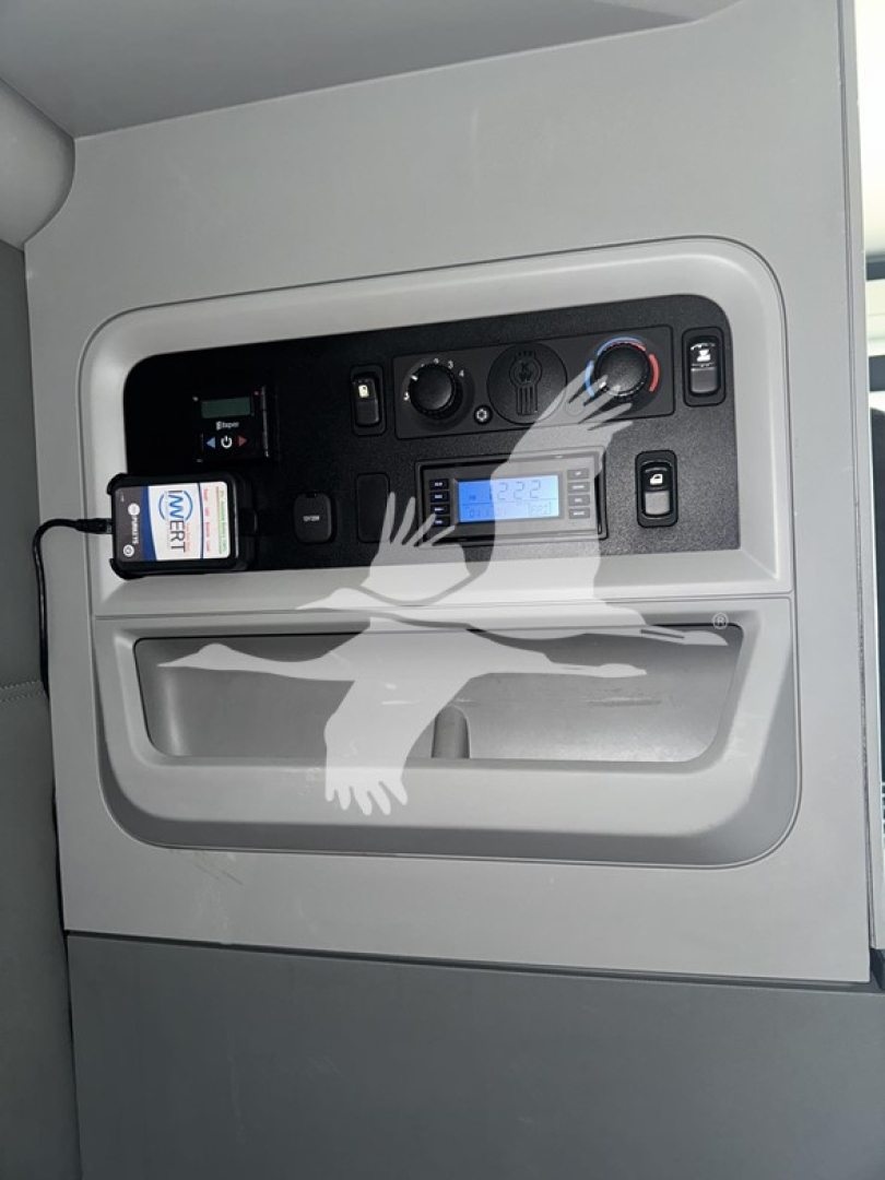 Truck cab interior panel showing control gauges and electronics; USB/ECU-style unit plugged into a socket, buttons and LCD display visible.