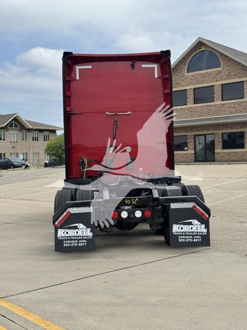 Back of red Kenworth trailer chassis with fifth wheel and rear lights, two Kordell mud flaps, and asphalt lot in background.