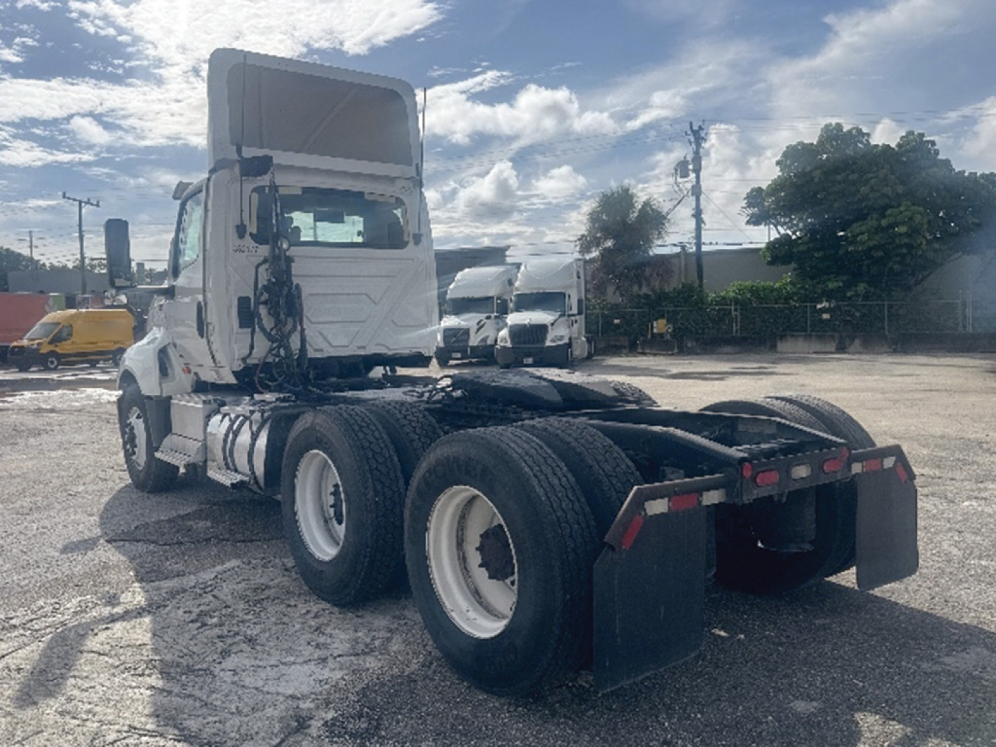 Truck chassis and cab rear view showing dual rear axles and fifth-wheel/landing gear area, with white cab and black mud flaps.