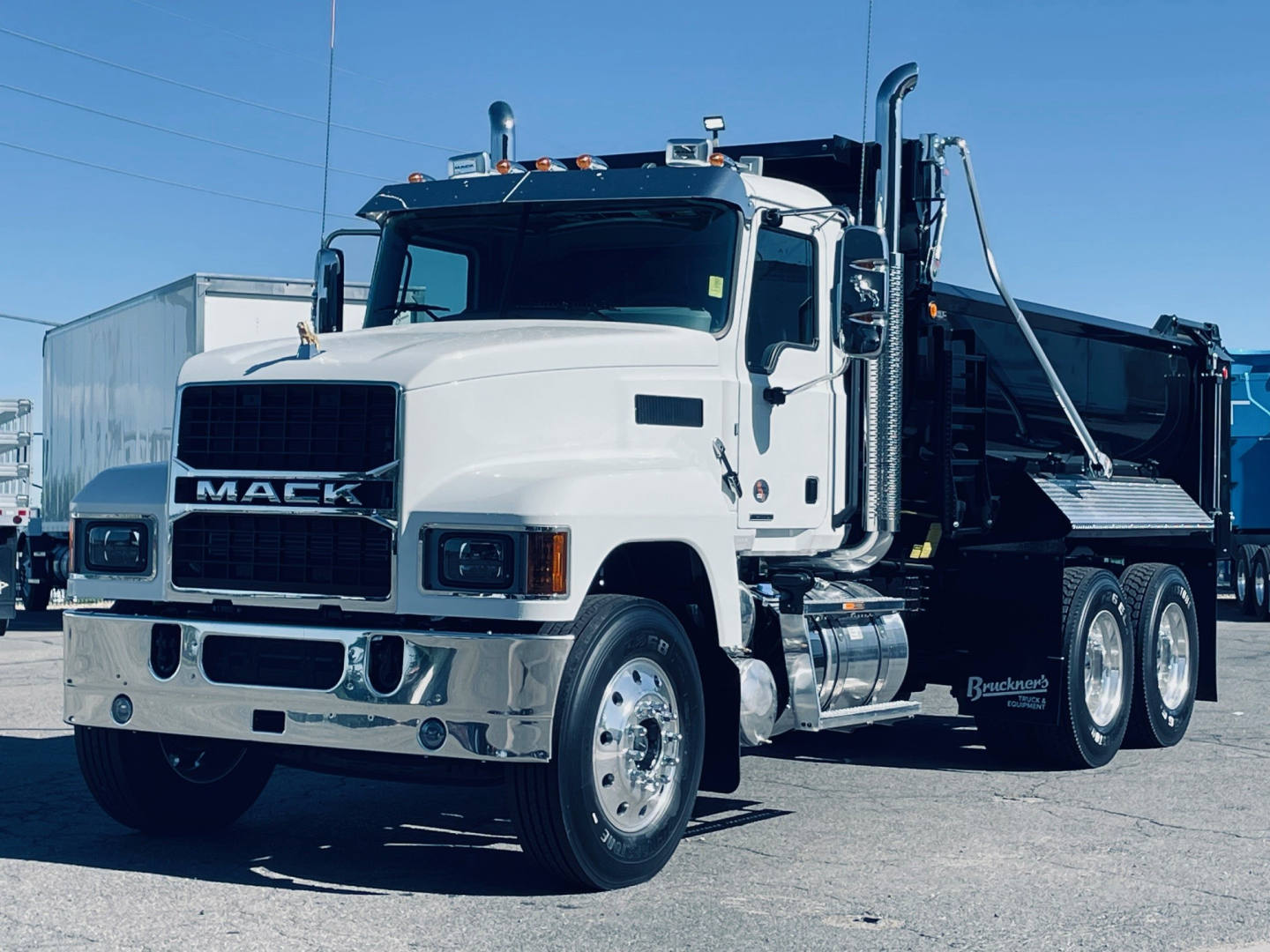 2026 Mack PI64 dump truck in white with Mack grille, dual exhaust stacks, and dump bed; side view showing cab, front bumper, and heavy-duty tires.