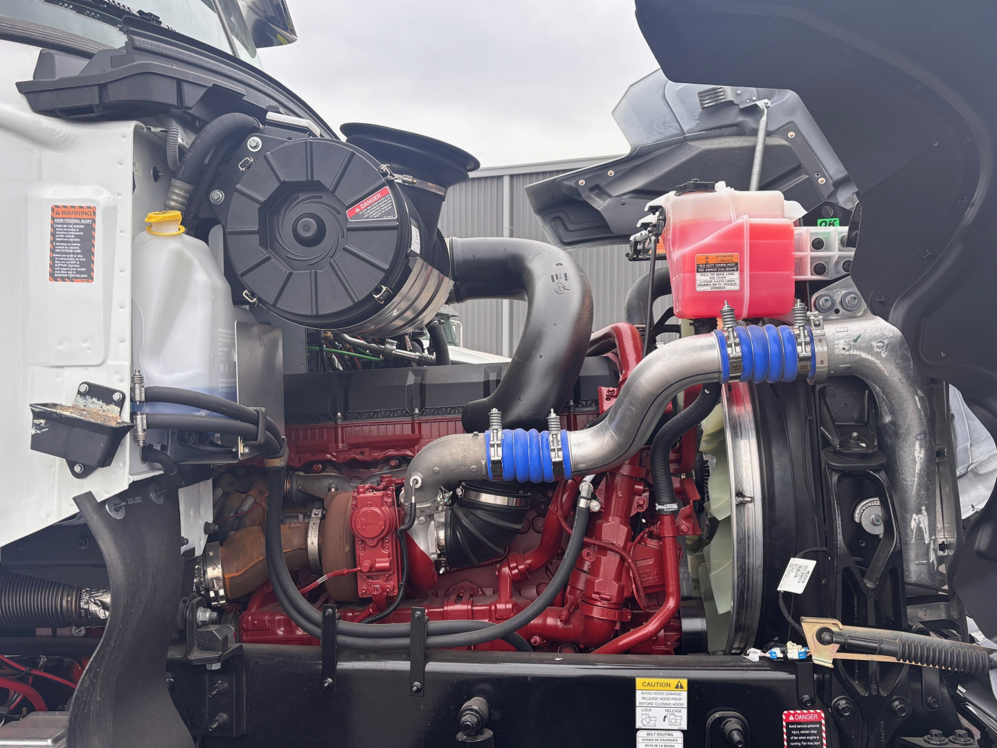 Mack PI64 engine bay showing red diesel engine with coolant reservoir, hoses, and radiator assembly.