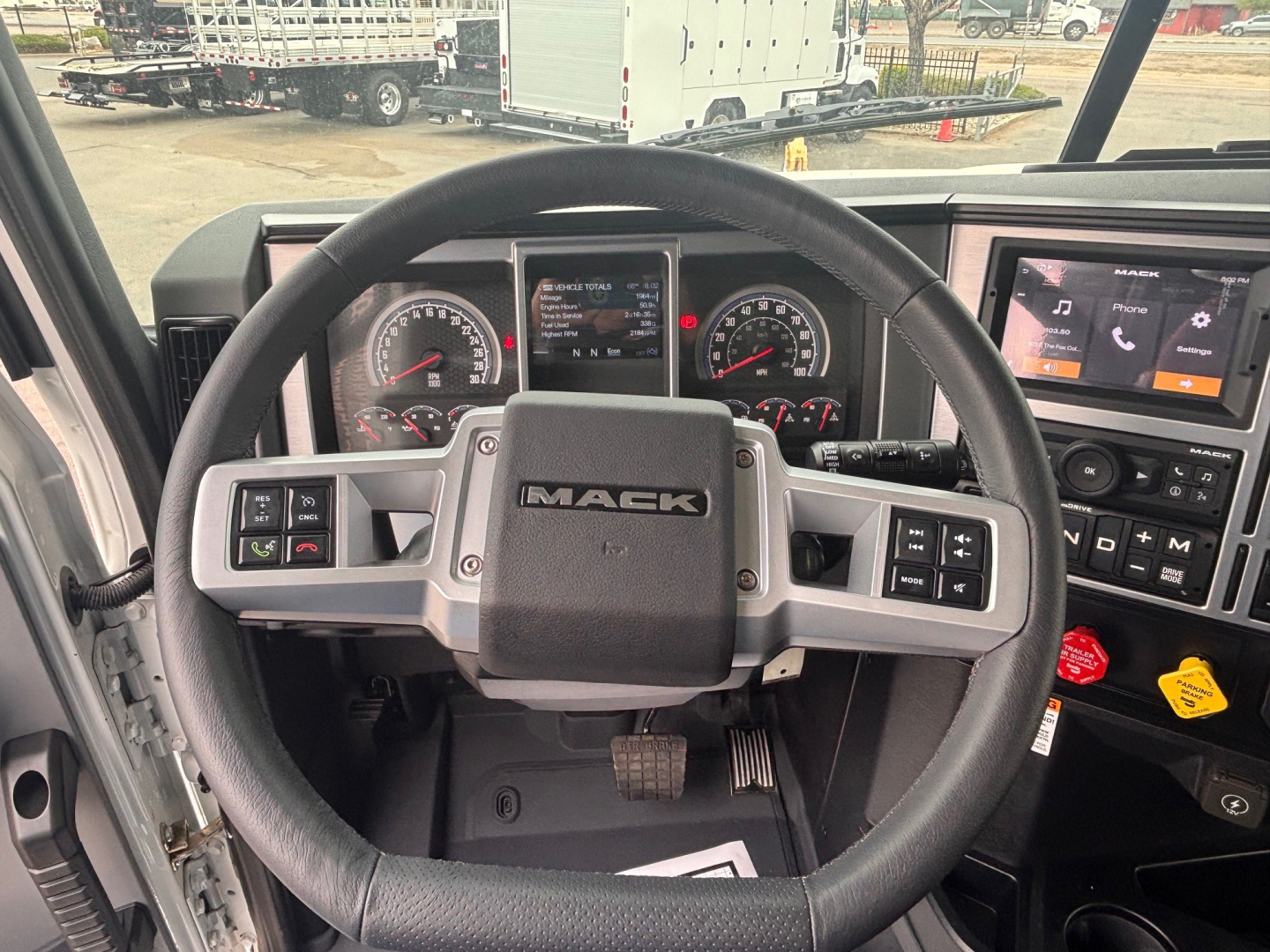 Mack PI64 cockpit steering wheel and dashboard with digital gauges, steering wheel logo, and center touchscreen display visible.