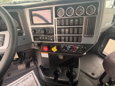 Mack PI64 dash panel showing instrument cluster, switches, and gear selector area with coolant and warning labels. Includes steering wheel left and cup holders under center console.