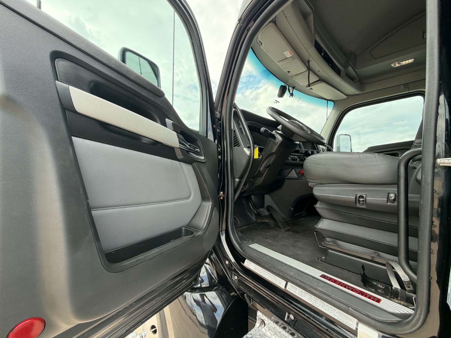 Kenworth T680 cab interior with open driver door showing steering wheel and grey seat, dashboard, and entry step.