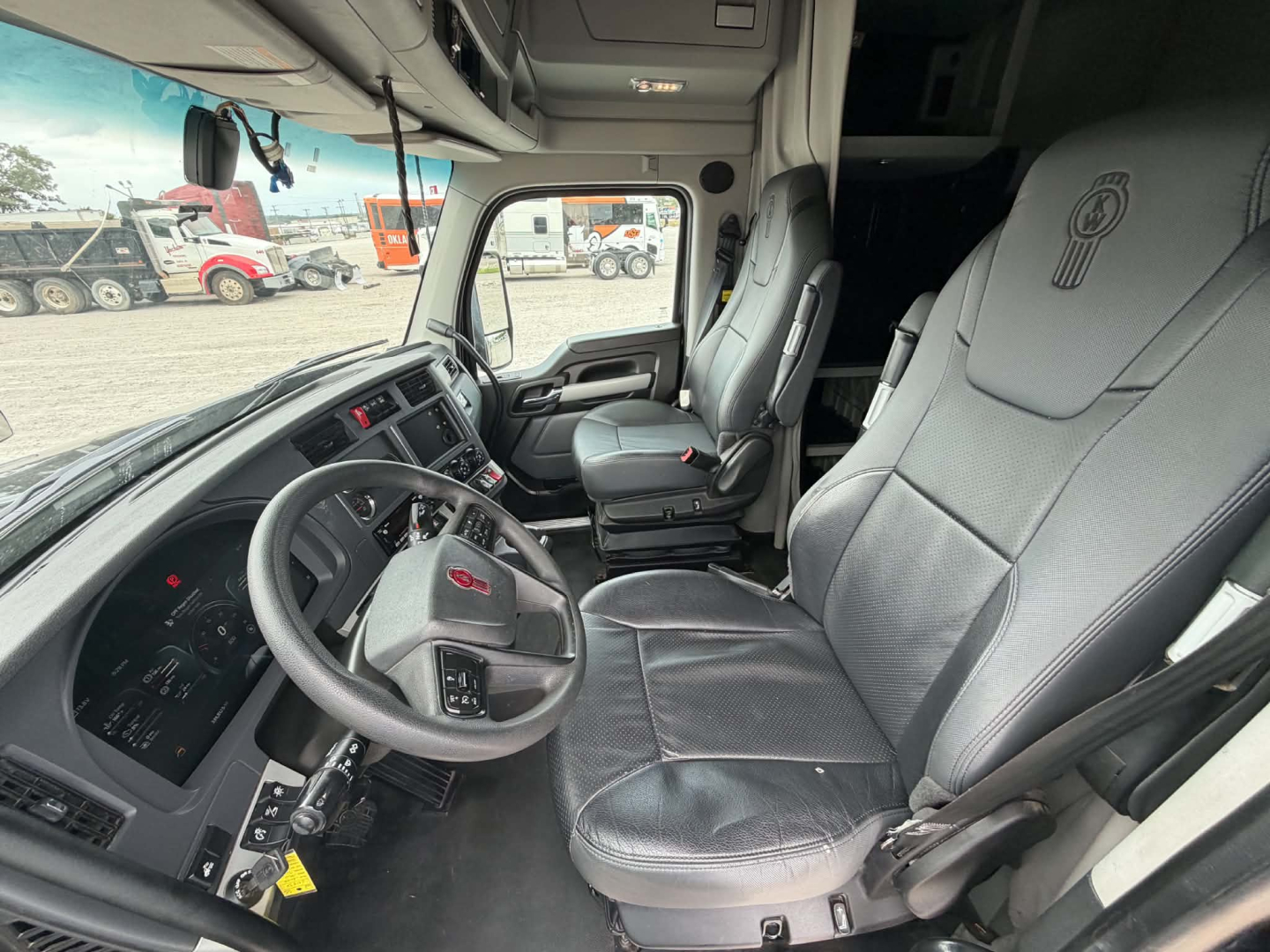 Kenworth T680 truck interior showing driver seat and passenger seat with steering wheel and dashboard; view through front windshield and side window.