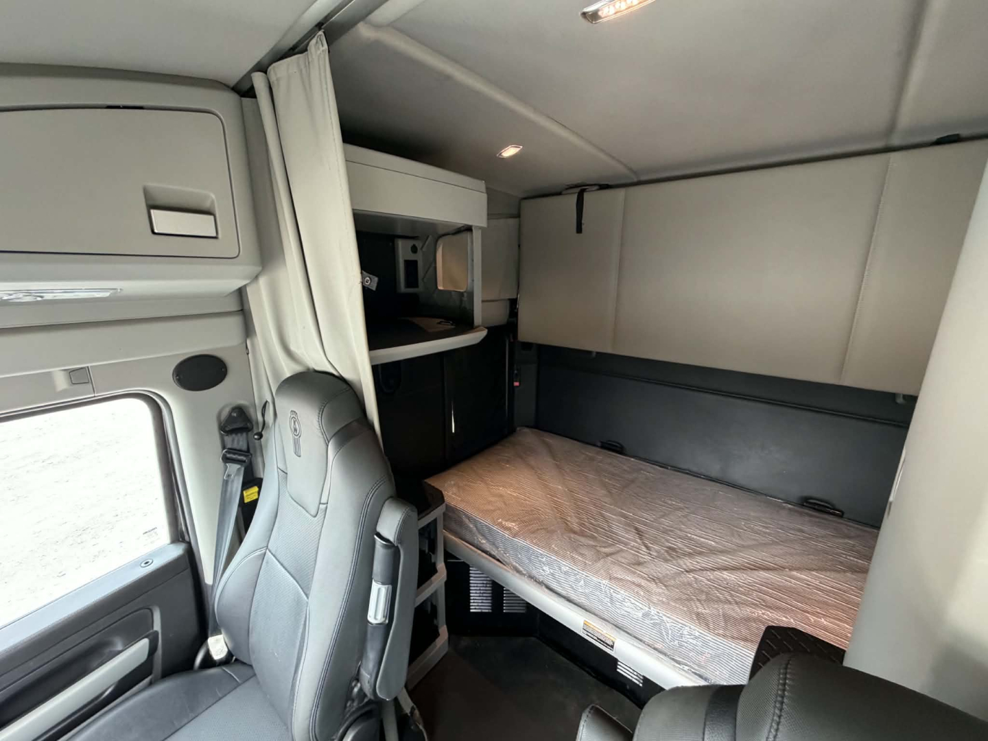 Truck cab sleeper area of a 2022 Kenworth T680 showing bunk bed with mattress, window, and storage compartments.