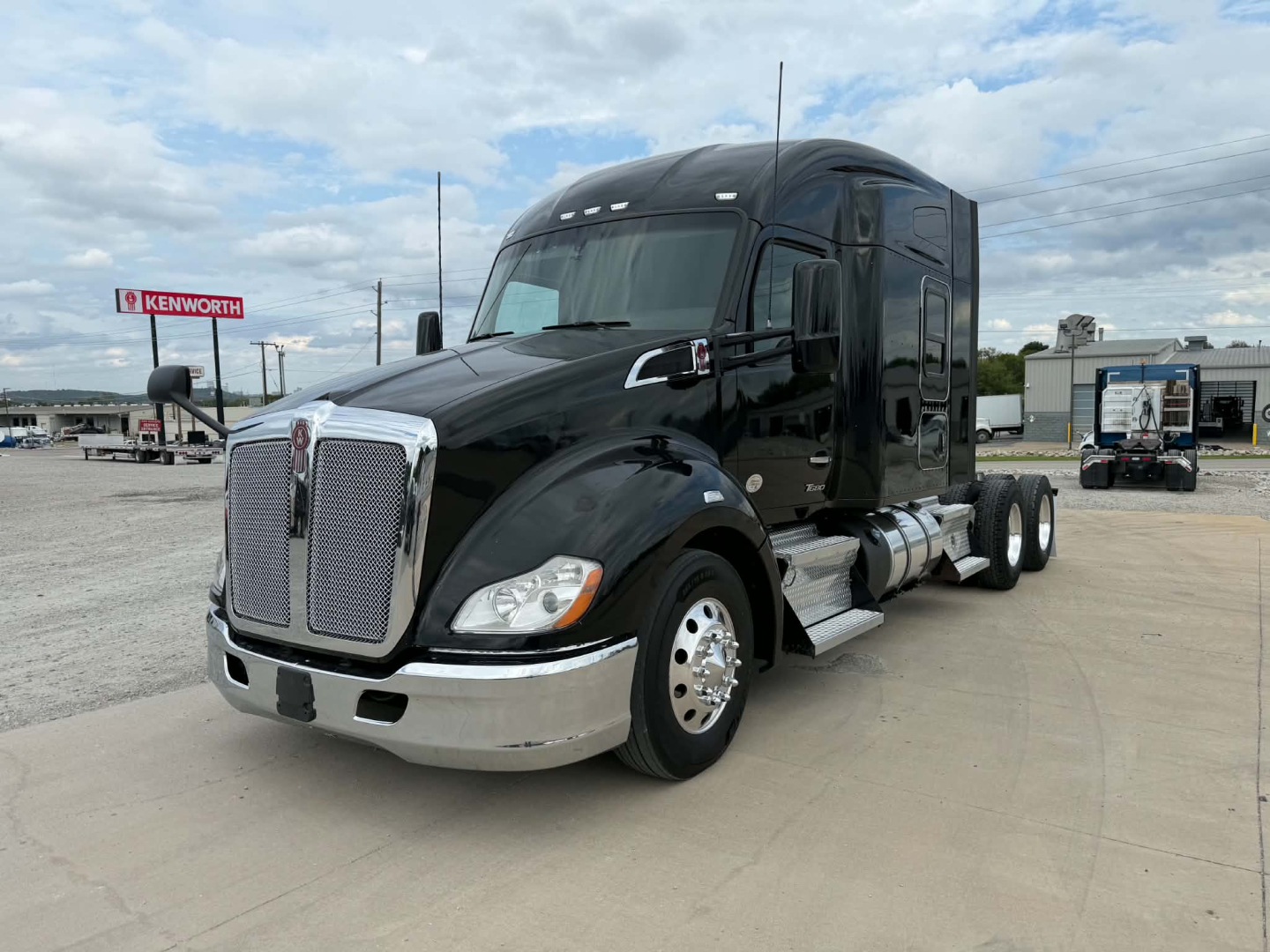 Kenworth T680 tractor trailer front-left view showing chrome grille, black cab, dual rear axles, and fuel tanks.