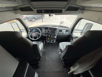 Kenworth T680 cab interior view from windshield angle with driver and passenger seats, dashboard with gauges and center console, steering wheel, overhead bunk area.