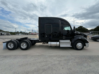 Kenworth T680 conventional sleeper truck side view showing dual rear axles and chrome fuel tanks, black paint, VIN plate area not visible.