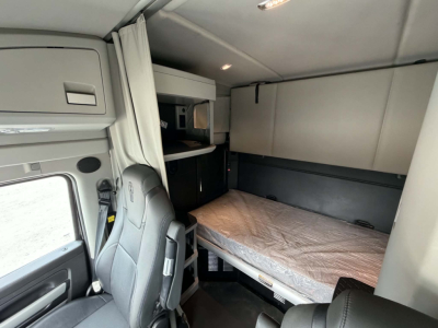 Truck cab sleeper area of a 2022 Kenworth T680 showing bunk bed with mattress, window, and storage compartments.