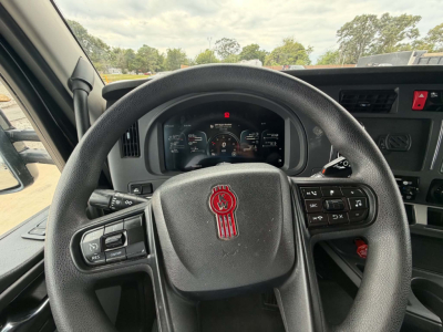 Kenworth truck steering wheel and dashboard showing steering wheel emblem and instrument cluster. Door controls visible on left, cruise control on right, no legible small text.
