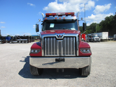 Western Star 49X truck front view showing large chrome grille, red cab, bumper, and surrounding yard with other trucks in background.