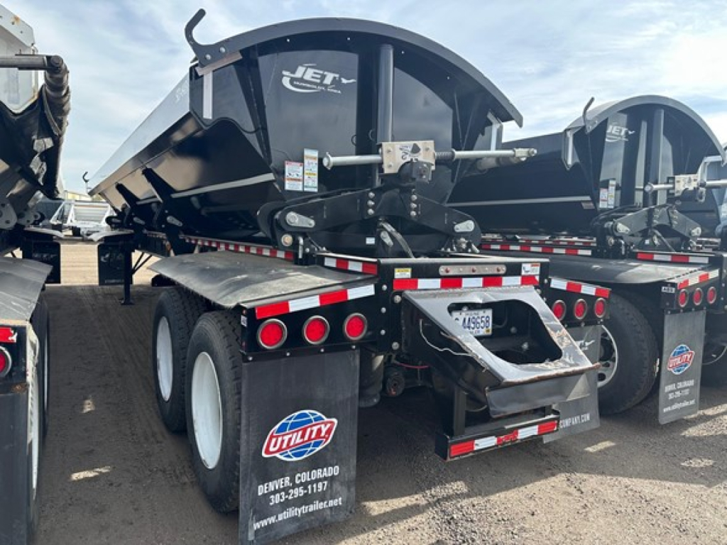 Jet air ride side dump trailer rear view showing black frame, dual axles, red and white reflective tape, Utility Denver logo mudflaps, and VIN plate area.
