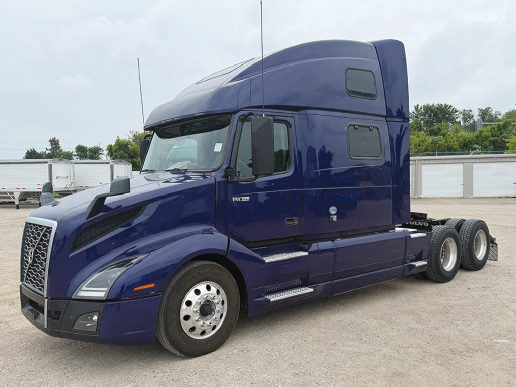 Variant Volvo VNL 860 truck with deep blue cab, sleeper, front grille, and dual rear axles. Closed storage units in background.