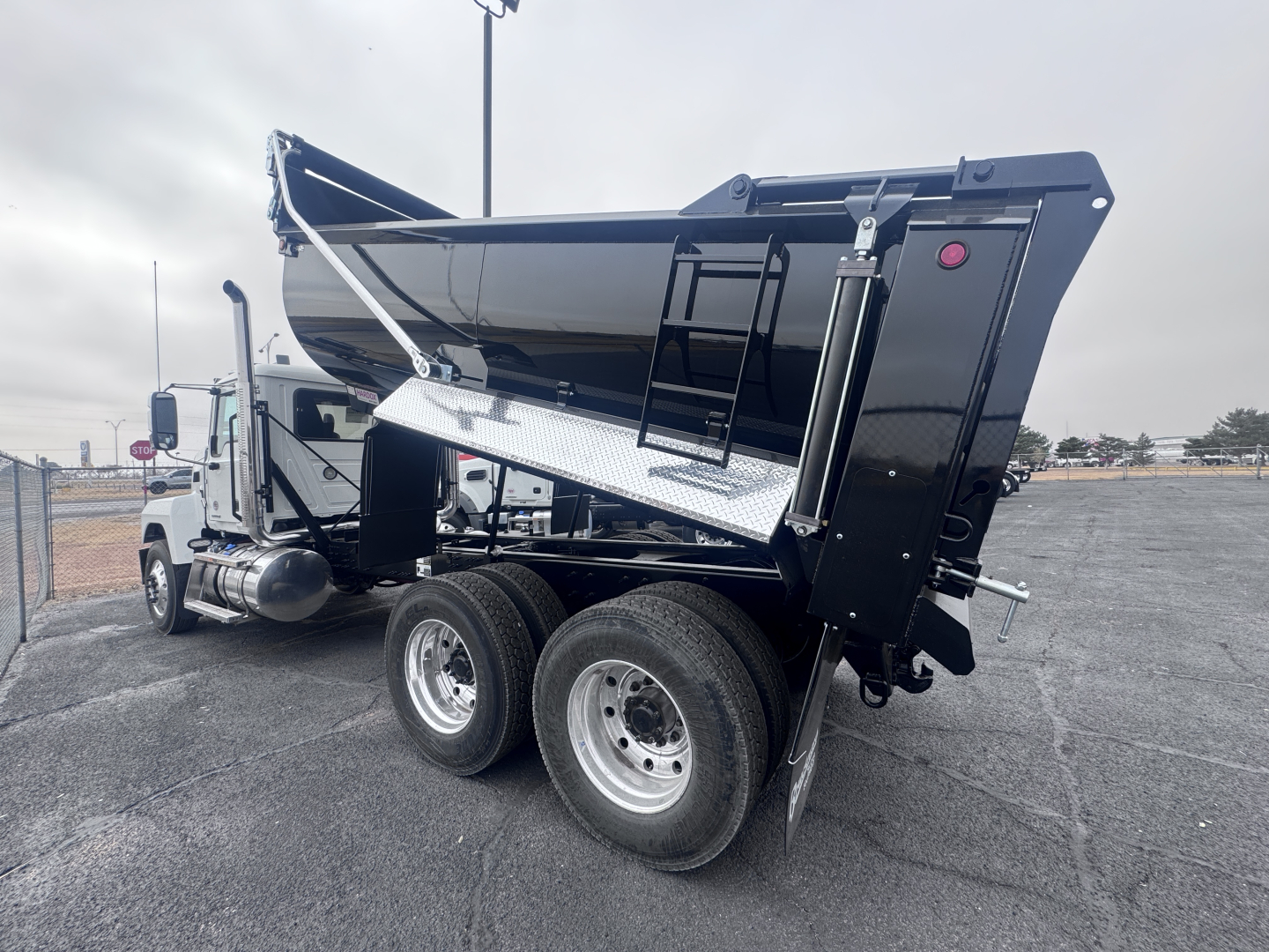 Truck chassis with dump bed raised showing dual rear axles and hydraulic lift, 2026 Mack PI64 dump truck in a parking lot.