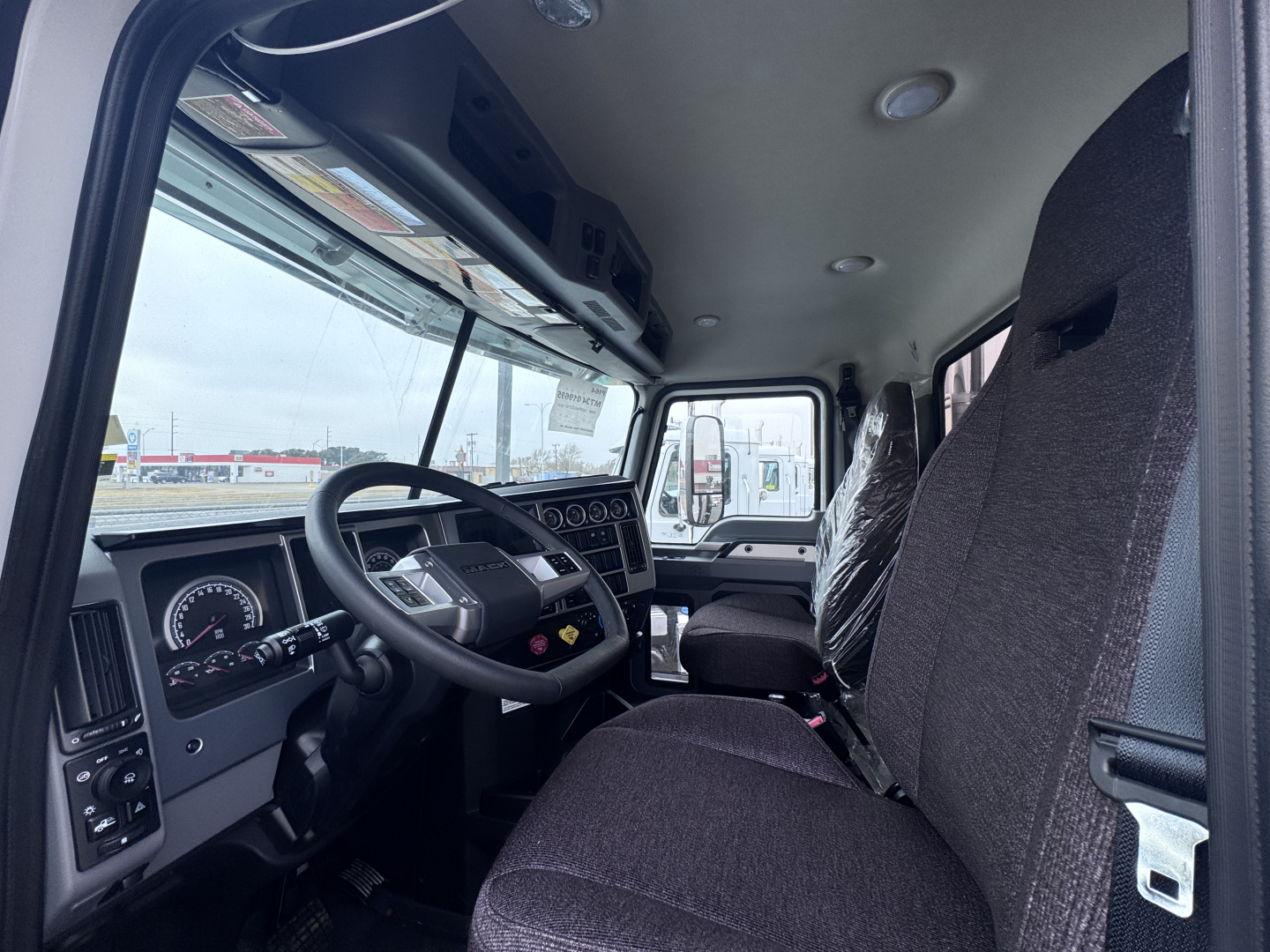 Dashboard and steering wheel of a 2026 Mack PI64 truck cab interior with dark fabric seats.