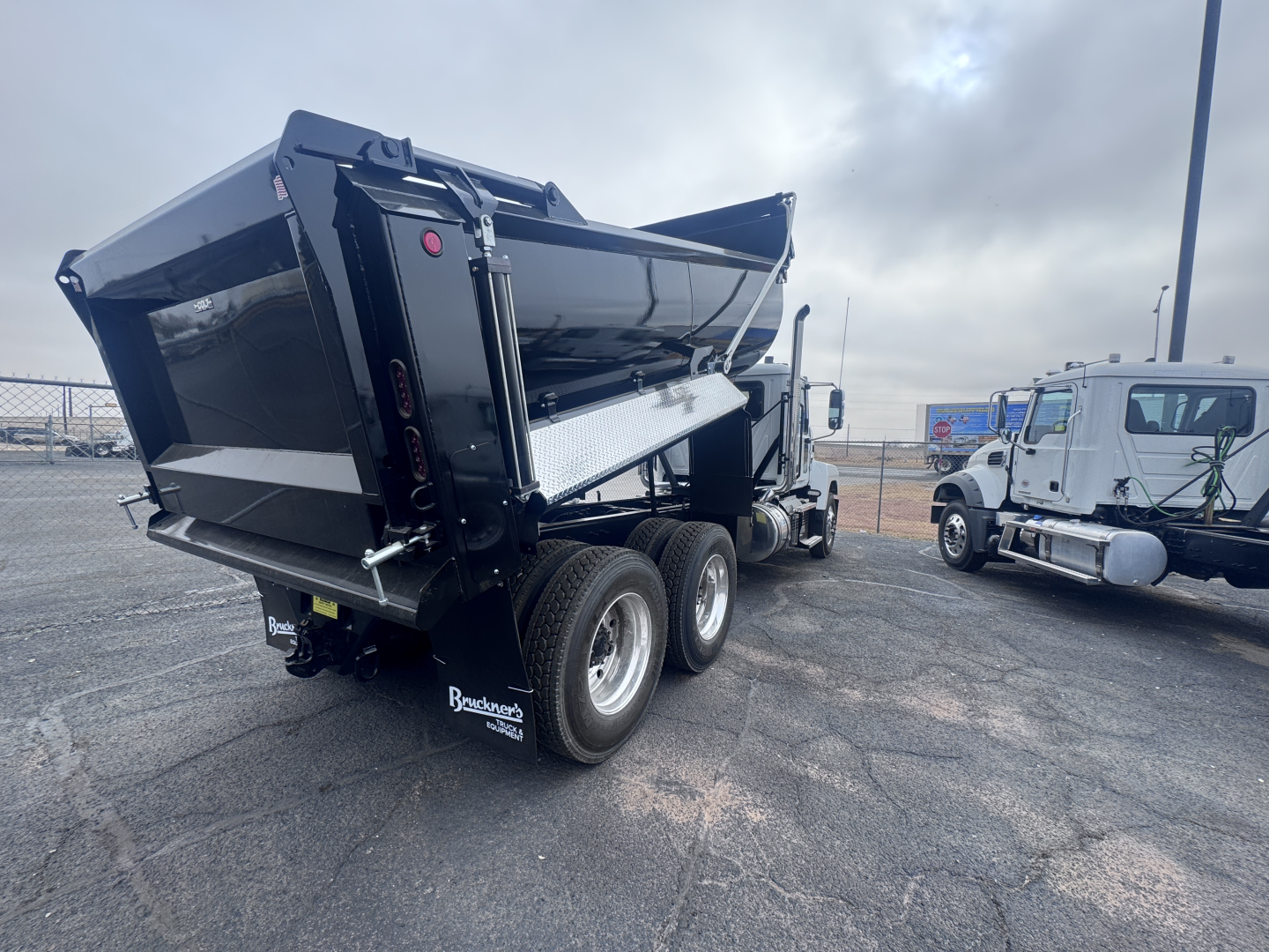 Dump truck bed of a new Mack PI64 with a raised black dump body and dual rear wheels, side ladder and reflective markings.