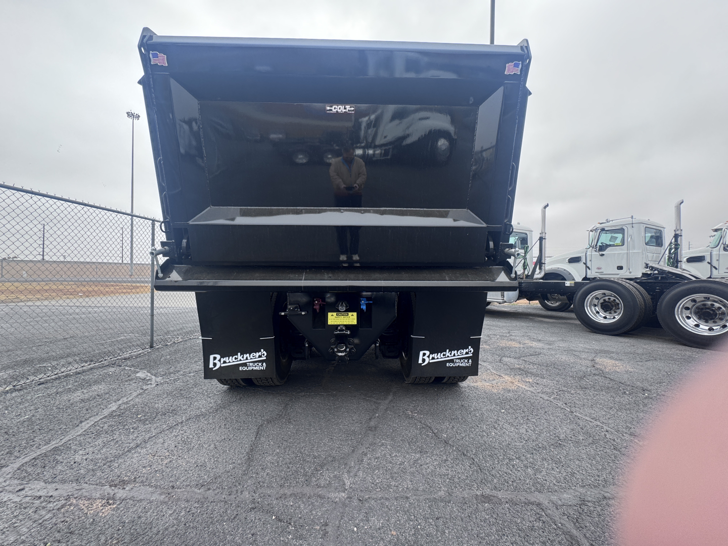 Mack PI64 dump truck rear view with raised dump bed, visible tailgate components, and Brackett stickers on mud flaps; yellow caution label and hydraulic mechanism visible.