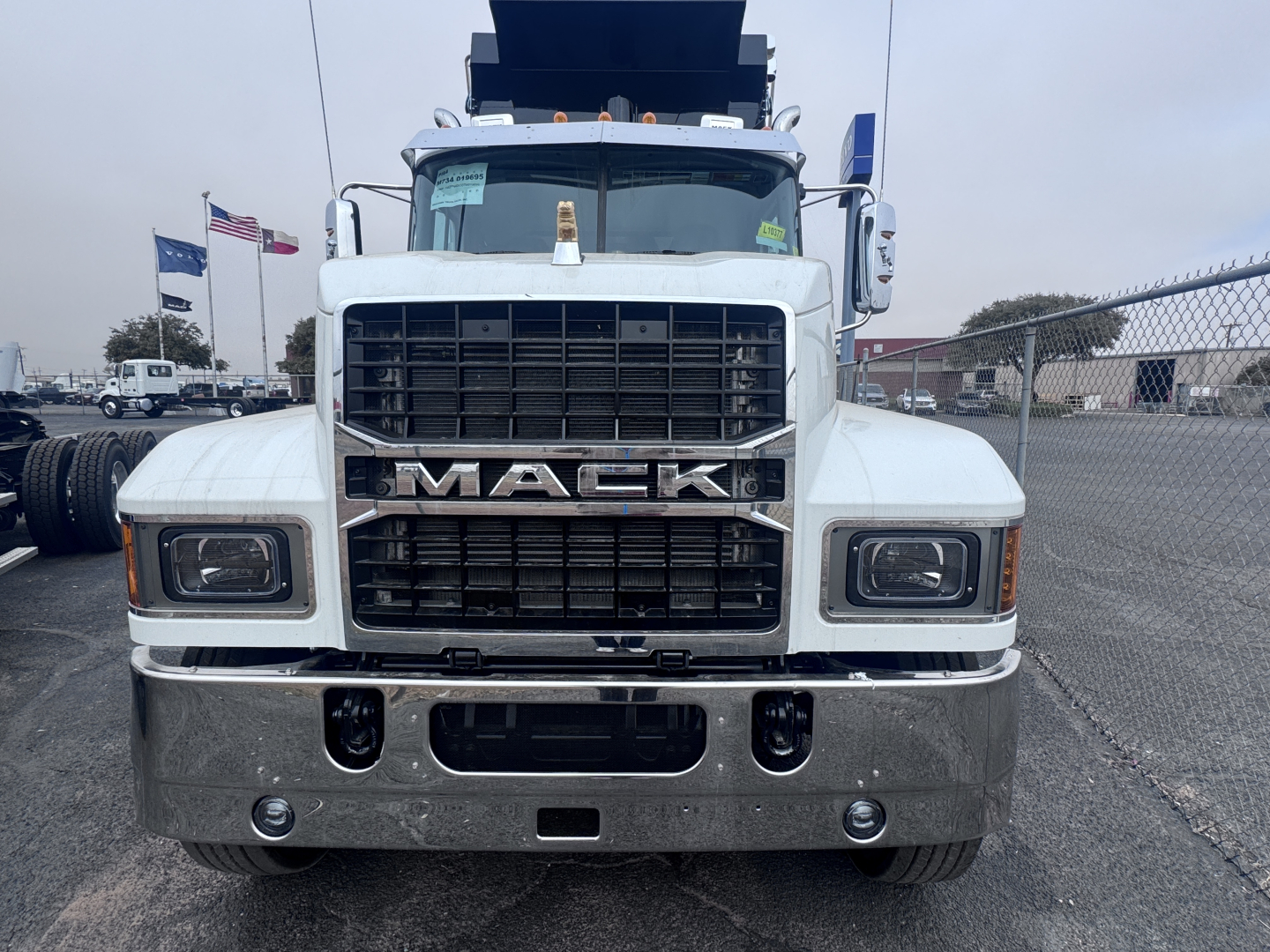 Front view of a white Mack PI64 dump truck with large grille, chrome bumper, and raised dump bed in the background.