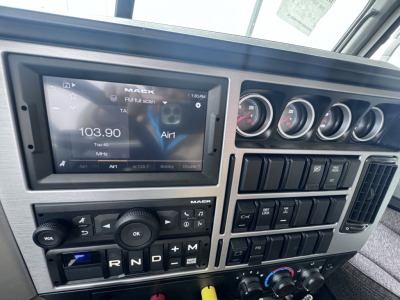 Mack PI64 dashboard showing touchscreen display with radio frequency 103.90, multiple gauges, gear selector, and control switches in the cab interior.