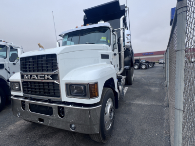 Mack PI64 dump truck in a lot showing front grille with MACK lettering, large chrome bumper, headlights, and dump bed raised. Visible text includes MACK on grille and truck body styling.