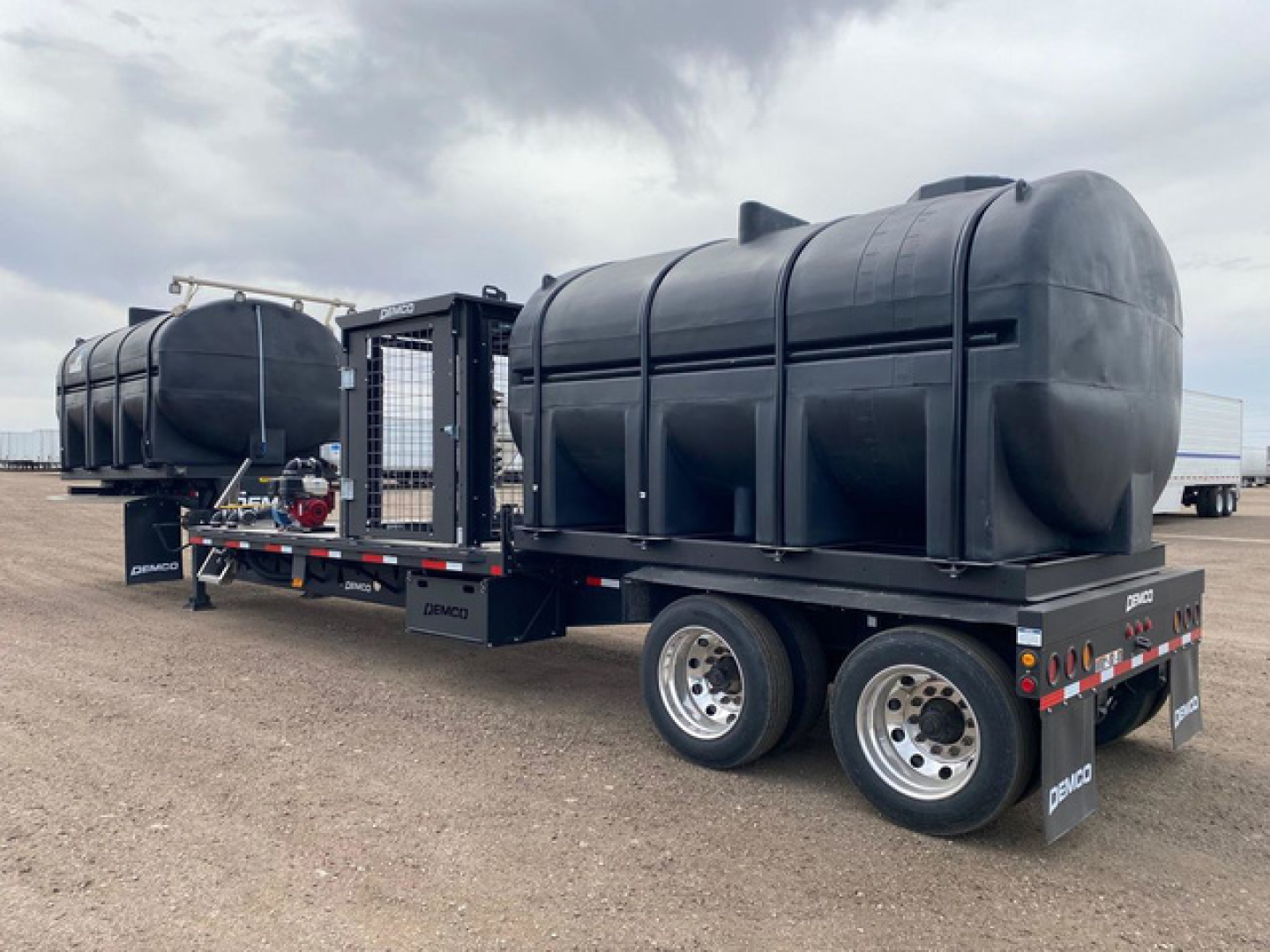 Demco liquid tender trailer with two large cylindrical tanks mounted on dual-axle trailer. Visible labels include Demco on the trailer frame and wheel guards.