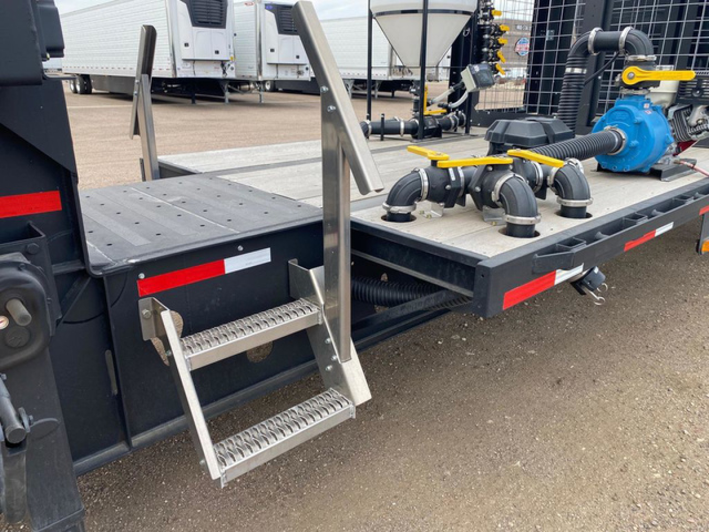 Trailer rear section showing a metal step ladder, platform, hoses, valves, and a blue pump on Demco Liquid Tender trailer.