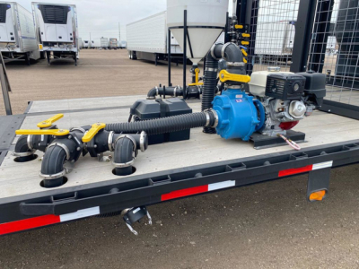 Demco Liquid Tender on trailer deck showing blue pump, yellow valves, hoses, and grey piping assembly.