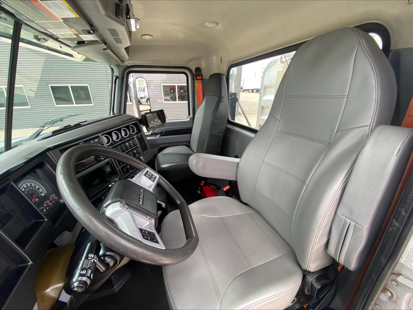 Cab interior of a 2019 Mack PI64T truck showing steering wheel, dashboard gauges, and grey driver and passenger seats.