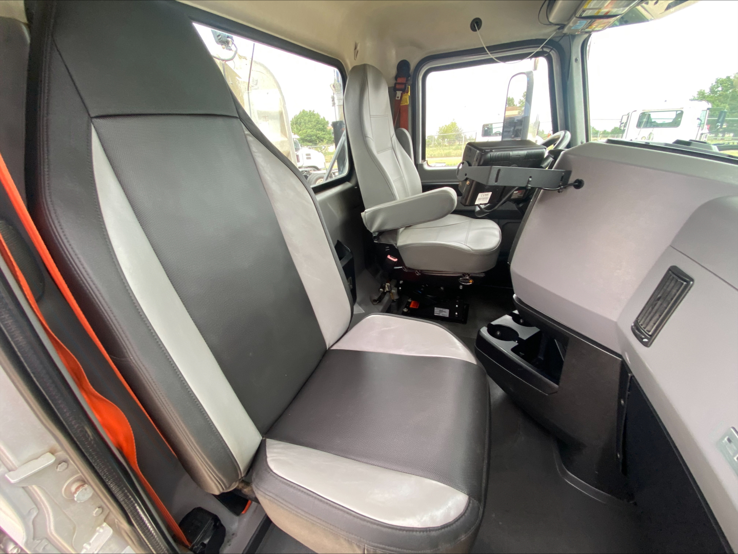 Truck cab interior of a 2019 Mack PI64T showing front bench and passenger seat with black and gray upholstery, dashboard, steering wheel, and center console.