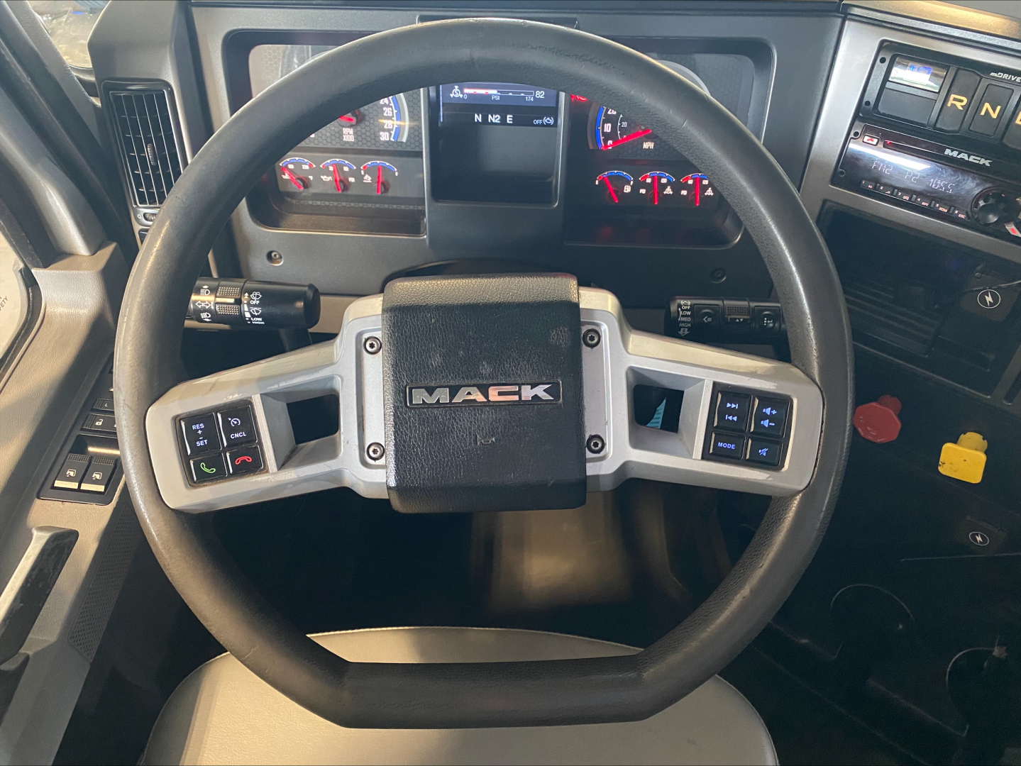 Steering wheel and dashboard of a 2019 Mack PI64T truck inside cab showing Mack badge on the center of the steering wheel.