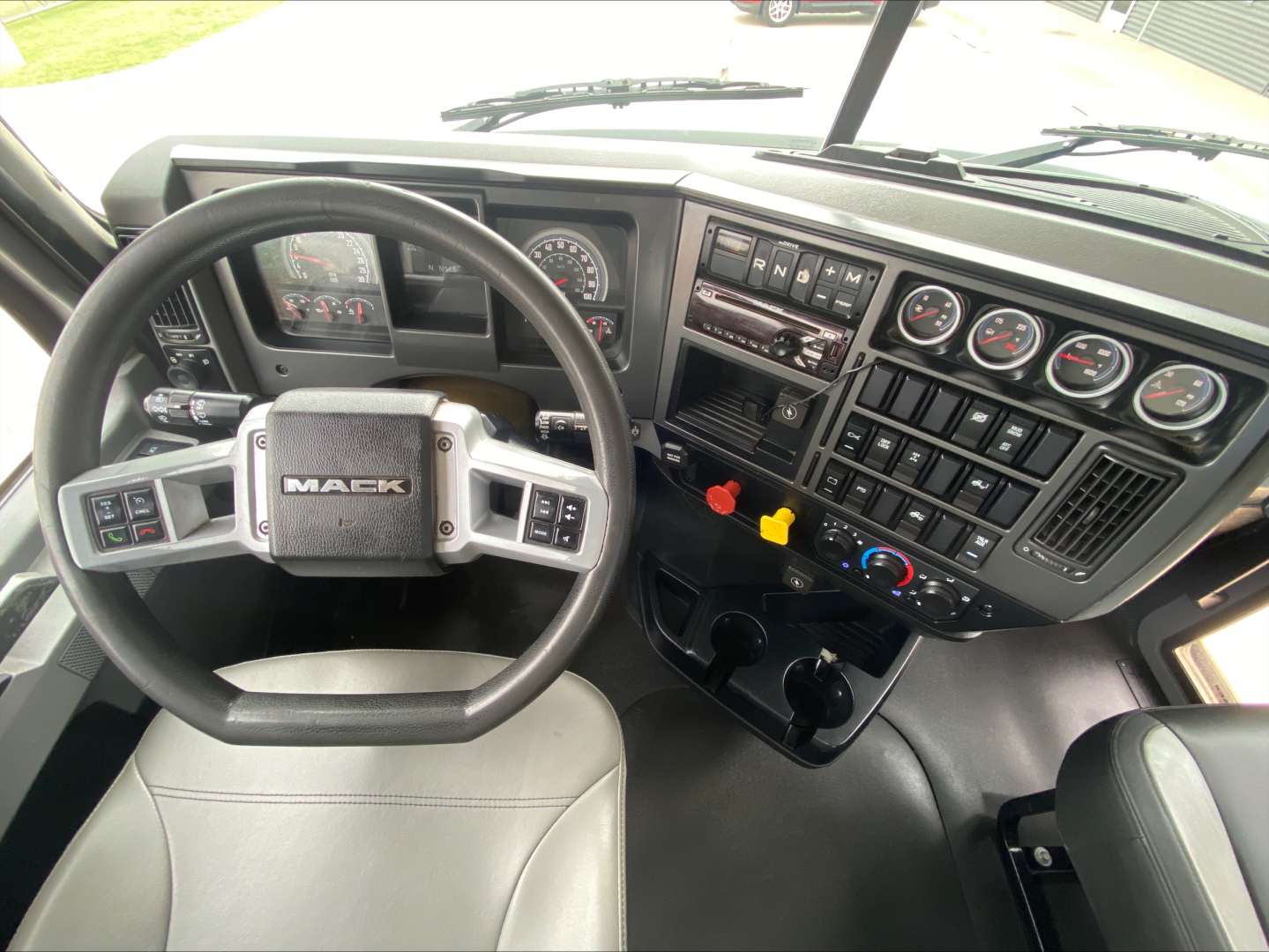 Mack PI64T cab interior showing steering wheel and instrument cluster with dashboard controls.