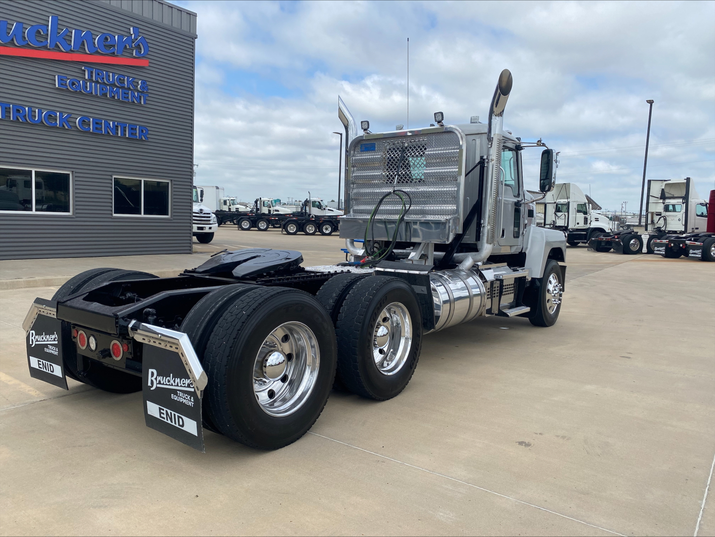 2019 Mack PI64T conventional daycab tractor seen from rear three-quarter view; dual rear axles with chrome fuel tanks, shiny wheels, and bumper mudflaps; visible dealership building in background.