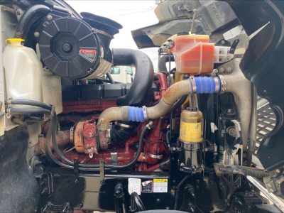 Engine bay of 2019 Mack PI64T daycab truck showing intake, coolant reservoir, hoses, and filters with visible red engine block and blue silicone hoses.