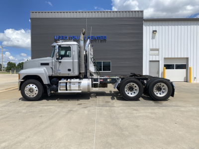 Truck side view of a 2019 Mack PI64T with a quad-axle configuration, parked in front of a used truck center building. Visible text includes 'USED TRUCK CENTER' on the building facade.