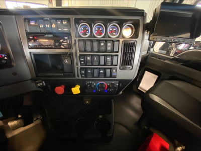 Dashboard view of a 2019 Mack PI64T truck showing gear selector, multiple gauges, control switches, and a mounted screen nav system.