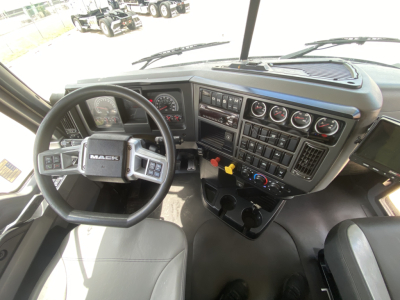 Mack PI64T truck cab interior showing steering wheel, dashboard with multiple gauges, switches, and control panels.