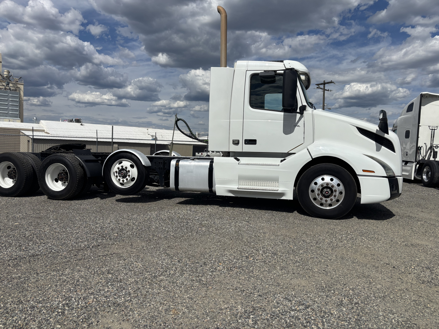 Truck side view showing a white Volvo VNL84 tractor cab with a tall exhaust stack, black chassis, and triple axles at rear.