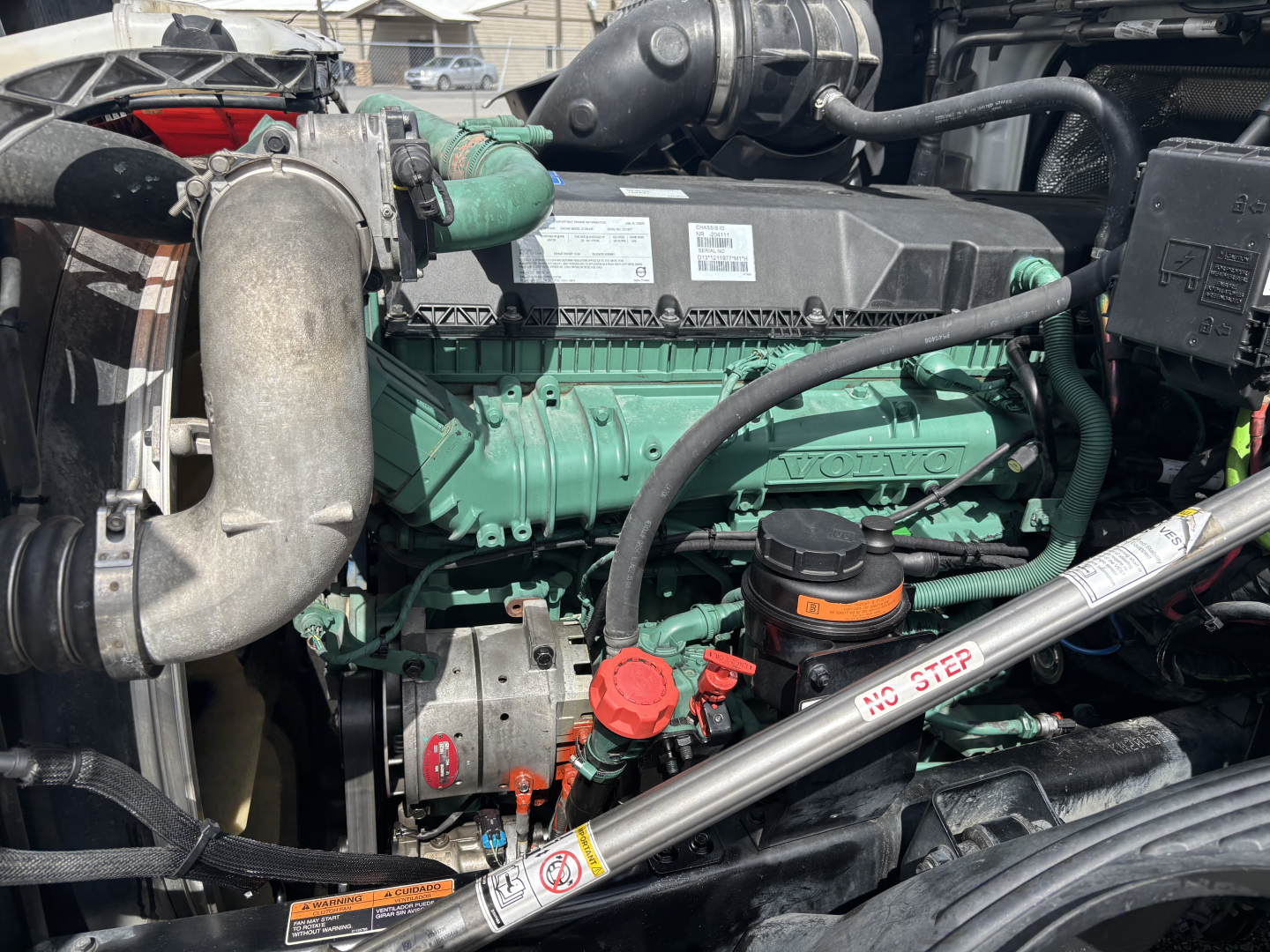 Volvo diesel engine bay with green engine block and surrounding components including coolant hoses, alternator, oil cap, and piping; label stickers and metal framework visible.