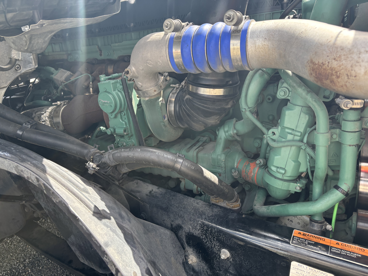 Volvo VNL engine bay with blue intake hose and green engine components. Visible labels and hoses, no dashboard text readable.