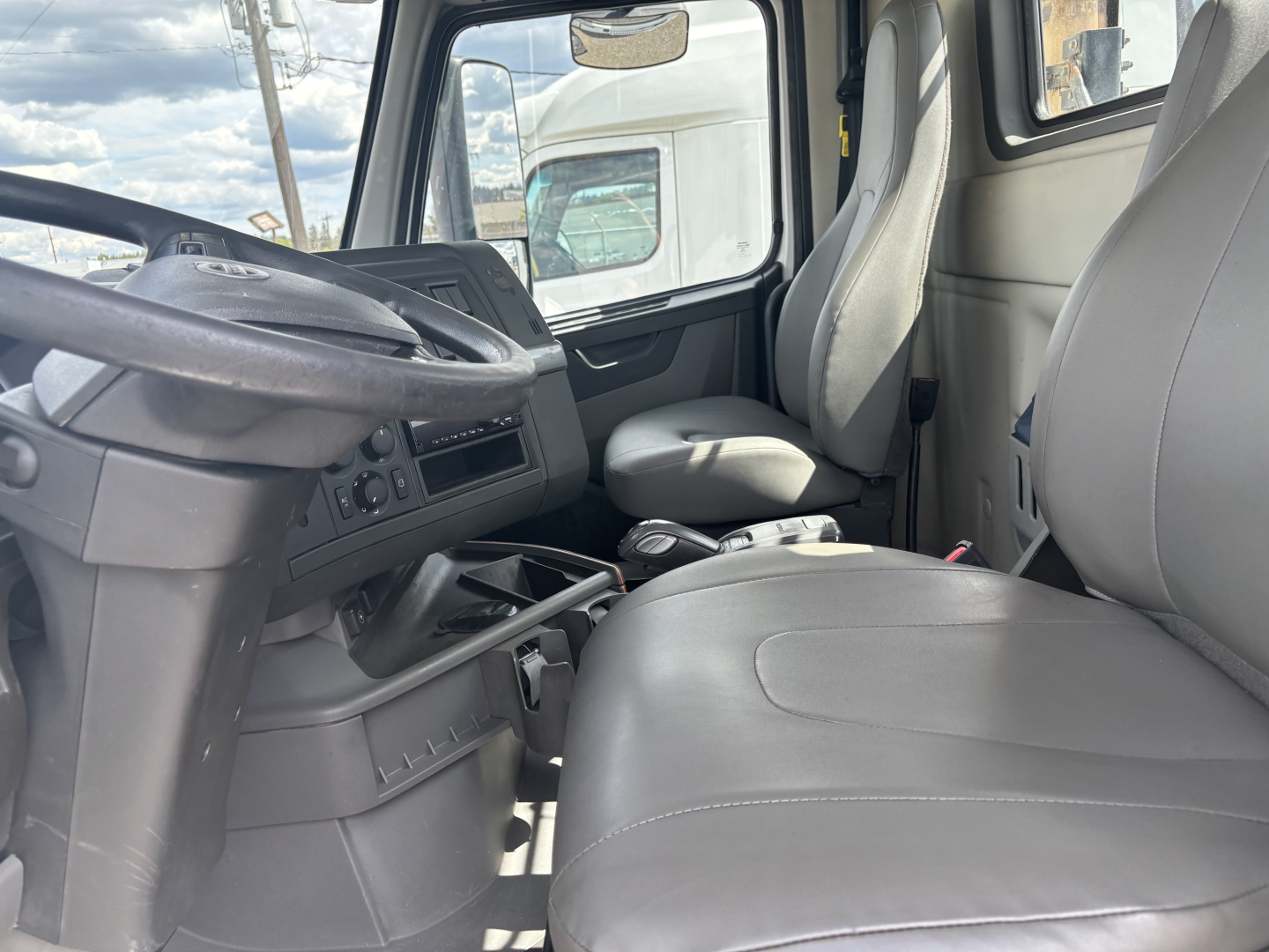 Volvo truck cab interior showing steering wheel, driver seat, and passenger seat with center console and dashboard controls.