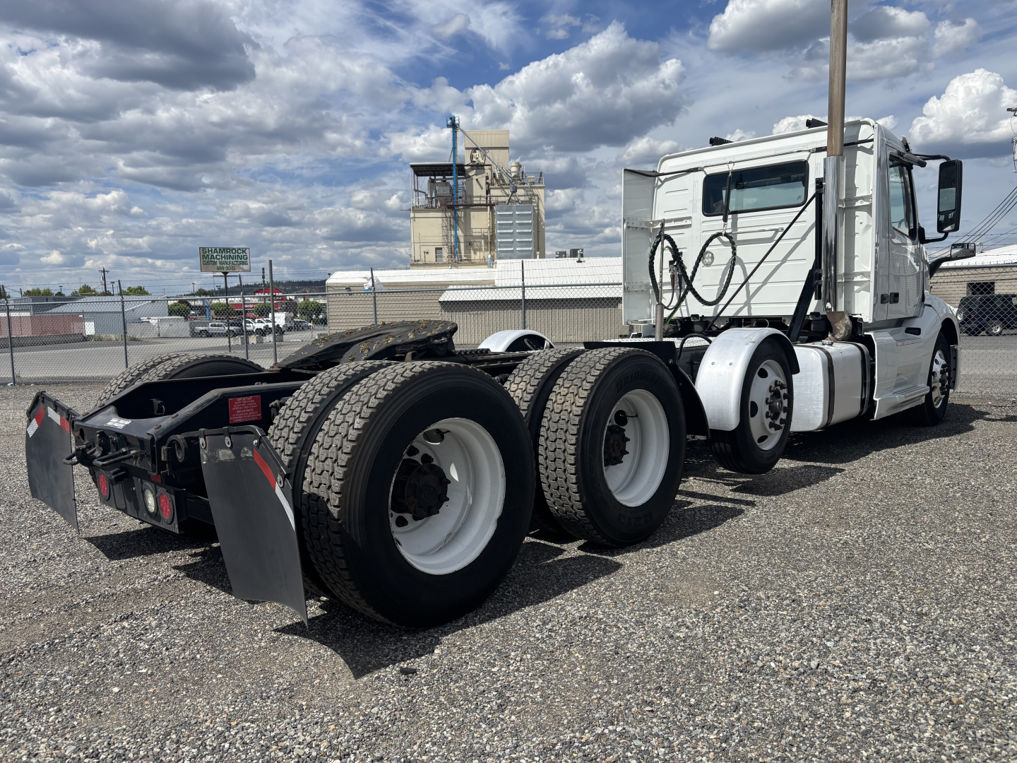 Volvo VNL cab with a triple axle rear, white exterior, long hood, side mirrors, and fifth wheel visible.