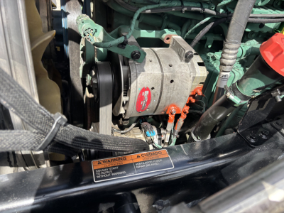 Volvo engine bay showing alternator with red label and surrounding green engine components and hoses.