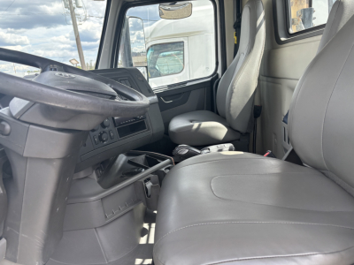 Volvo truck cab interior showing steering wheel, driver seat, and passenger seat with center console and dashboard controls.