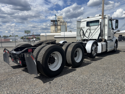 Volvo VNL cab with a triple axle rear, white exterior, long hood, side mirrors, and fifth wheel visible.