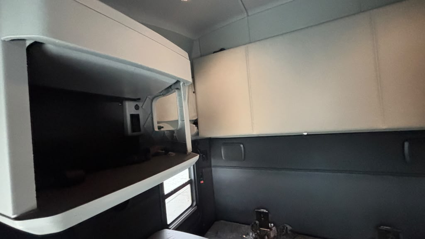 Cab interior of a truck cab showing a shallow storage shelf and window with a small red and white label.
